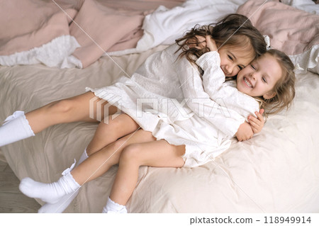 Two funny little sisters hug and laugh merrily while lying in bed. Children in nightgowns 118949914
