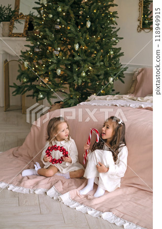 Children are playing with Christmas decorations in the bedroom by the Christmas tree. Waiting for the new Year 118949915