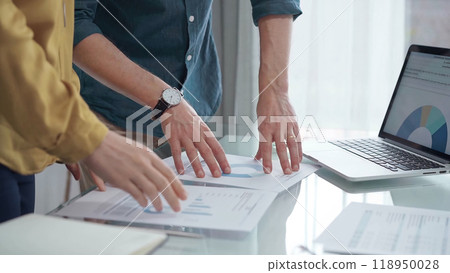 Business people, professionals analyzing financial charts and data on a desk while standing and using laptop computer in office Business people, professionals analyzing financial charts and data on a desk while standing and using laptop computer in office 118950028