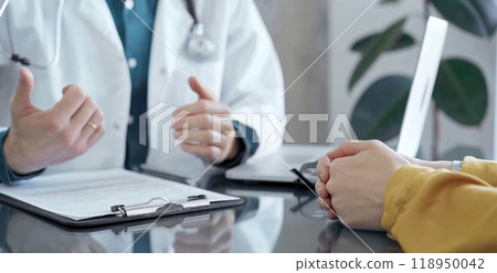 Doctor and patient consultation in clinic. Patient listens attentively as a doctor explains a diagnosis in a modern medical office, close up. Medicine and health care 118950042