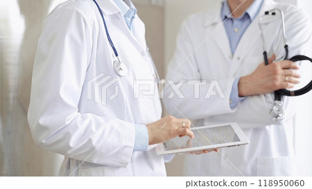 Two doctors wearing white coats and stethoscopes, using a digital tablet, discussing a patient's medical history. Medicine and science Two doctors wearing white coats and stethoscopes, using a digital tablet, discussing a patient's medical history. Medicine and science 118950060