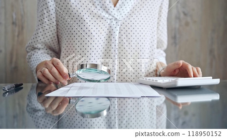 Auditor woman analyzing financial documents with magnifying glass and calculator at her office desk in formal white blouse with polka dots. Business people concept Auditor woman analyzing financial documents with magnifying glass and calculator at her office desk in formal white blouse with polka dots. Business people concept 118950152