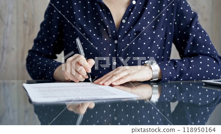 Businesswoman is signing corporate contract at her office desk in formal dark blue blouse with polka dots. Business people concept Businesswoman is signing corporate contract at her office desk in formal dark blue blouse with polka dots. Business people concept 118950164