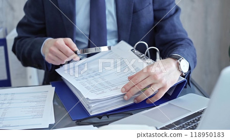 Adult businessman or auditor examining documents with magnifying glass. Professional in a suit scrutinizes financial reports, detail-focused work concept 118950183