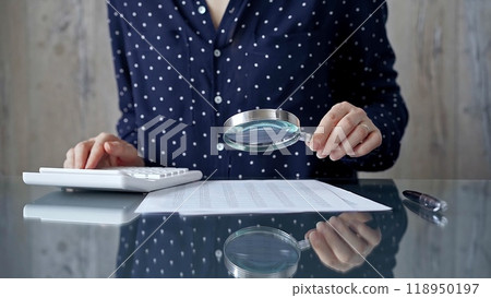 Auditor woman analyzing financial documents with magnifying glass and calculator at her office desk in formal dark blue blouse with polka dots. Business people concept 118950197