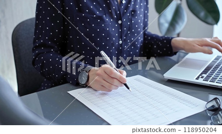 Businesswoman professional writing in a notebook beside a laptop at a modern workplace, close up view. Business concept 118950204