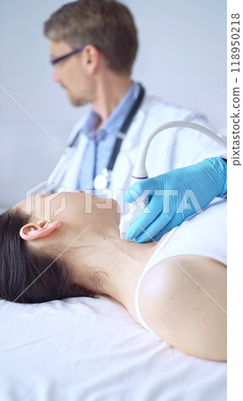 Doctor man wearing blue protective gloves is using ultrasound equipment on the neck of a patient woman, lying for examination. Medicine concept 118950218