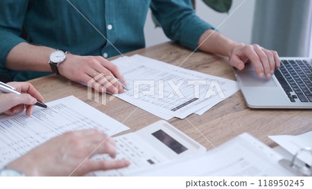 Auditor man wearing green shirt is reviewing papers and using a laptop with the colleague. Business people professionals analyzing financial documents. Finance, audit, and taxes 118950245