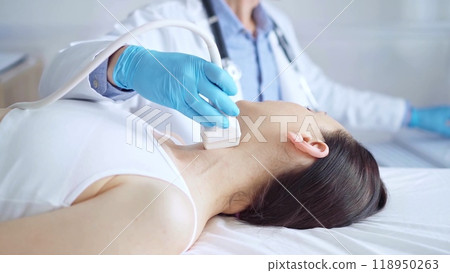 Doctor man wearing blue medical gloves is using ultrasound equipment on neck of female patient lying down for a medical examination 118950263