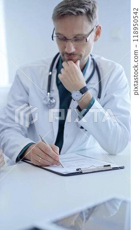 Doctor and a patient. The physician, wearing a white medical coat over a green shirt, gesturing with his hands during a consultation in the clinic. Medicine concept 118950542