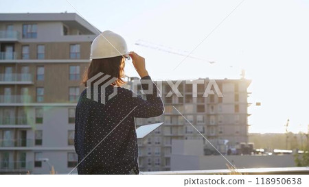 Female architect wearing a safety helmet is using a tablet computer while inspecting a building construction site at sunset Female architect wearing a safety helmet is using a tablet computer while inspecting a building construction site at sunset 118950638