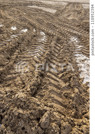 plowed soil covered with snow and frost in a field with tractor tracks 118952394