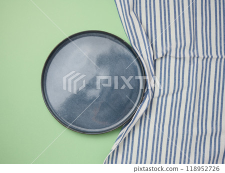Empty round ceramic plate and blue kitchen towel on green background, top view 118952726