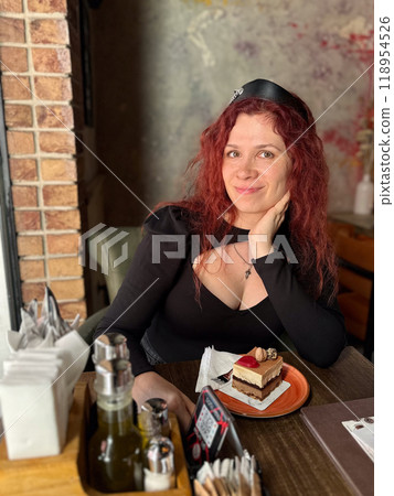 Millennial woman with red hair sits thoughtfully at a rustic cafe table, surrounded by a cozy and artistic atmosphere. Soft lighting and her pensive expression convey a sense of introspection and Millennial woman with red hair sits thoughtfully at a rustic cafe table, surrounded by a cozy and artistic atmosphere. Soft lighting and her pensive expression convey a sense of introspection and 118954526
