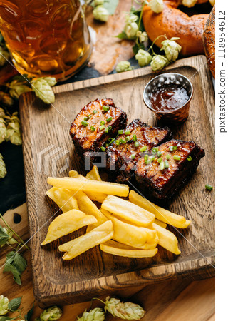 Close-up of barbecue ribs with crispy fries on a wooden board, served with a side of dipping sauce Close-up of barbecue ribs with crispy fries on a wooden board, served with a side of dipping sauce 118954612