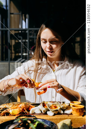 Young woman peeling shrimp at seafood restaurant, perfect for food lifestyle and dining out content Young woman peeling shrimp at seafood restaurant, perfect for food lifestyle and dining out content 118954632