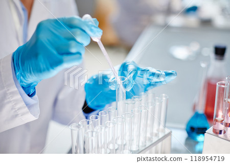 Close up on gloved hands of unrecognizable lab worker dripping liquid from dropper into test tube making reaction while developing new pharmaceuticals in laboratory, copy space 118954719