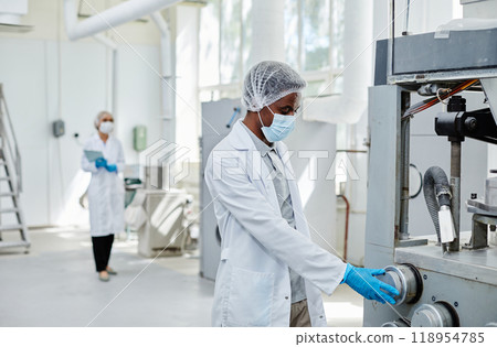 Side view of professional African American male production supervisor inspecting manufacturing machine controlling process quality and safety at pharmaceutical plant, copy space 118954785