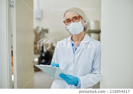 Waist up portrait of female process technician in lab coat taking notes in notepad while monitoring production at modern pharmaceutical manufacturing plant, copy space 118954817