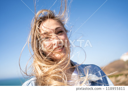 Smiling woman with tousled blond hair against blue Smiling woman with tousled blond hair against blue 118955811