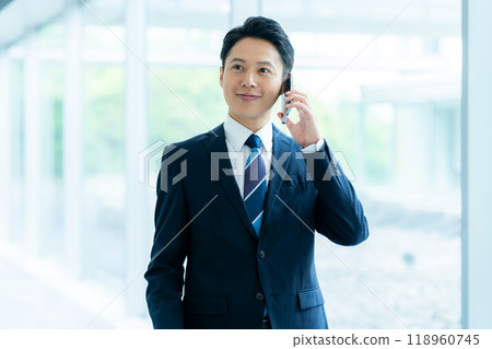 A businessman operating a smartphone in an office corridor 118960745