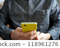A person holding a yellow smartphone with both hands. Facing forward. An image of someone calmly operating a smartphone. 118961276