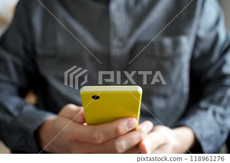 A person holding a yellow smartphone with both hands. Facing forward. An image of someone calmly operating a smartphone. A person holding a yellow smartphone with both hands. Facing forward. An image of someone calmly operating a smartphone. 118961276