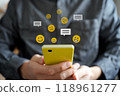 On top of the smartphone are emojis with various facial expressions, such as smiling faces, and speech bubbles for messages. 118961277