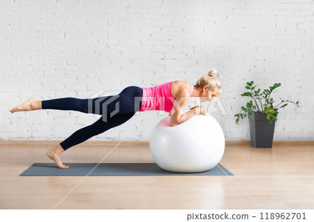 Fit adult woman in pink tank top practice elbow plank exercise with one leg up using fitness ball in loft studio indoor. Fit adult woman in pink tank top practice elbow plank exercise with one leg up using fitness ball in loft studio indoor. 118962701
