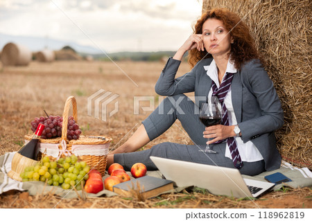 Woman in business suit spend time in field, settles down in nature with laptop and glass of wine 118962819