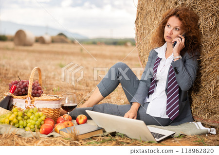 Woman in business suit spend time in field, settles down in nature with laptop and glass of wine 118962820