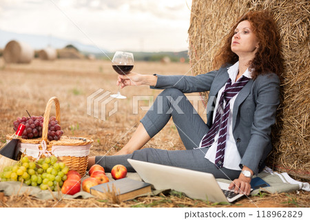Woman in business suit spend time in field, settles down in nature with laptop and glass of wine Woman in business suit spend time in field, settles down in nature with laptop and glass of wine 118962829