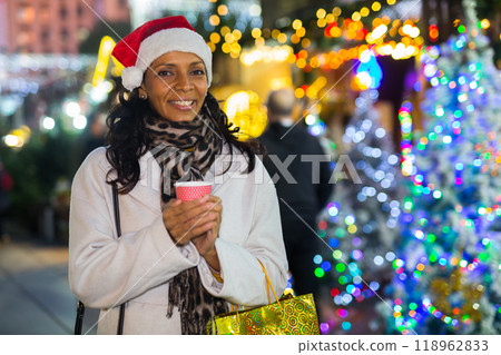 Happy woman with coffee over christmas tree lights outdoors Happy woman with coffee over christmas tree lights outdoors 118962833