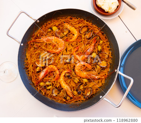 Appetizing traditional Spanish dish from prawns, mussels and noodles in a pan close to souse and glass of wine 118962880