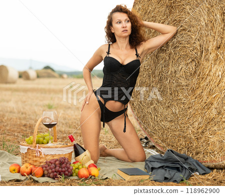 Woman in black corset lingerie and string panty sitting near haystack 118962900