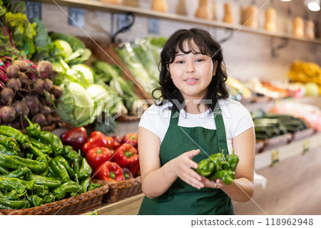 Smiling young saleswoman holding peppers in grocery store Smiling young saleswoman holding peppers in grocery store 118962948