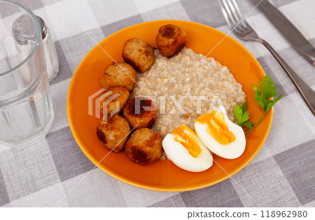 Homemade breakfast is served on plate - small portion of oatmeal, stewed meatballs and boiled egg Homemade breakfast is served on plate - small portion of oatmeal, stewed meatballs and boiled egg 118962980
