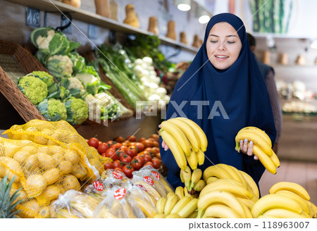 Pleased young Muslim woman purchaser choosing bananas in grocery store Pleased young Muslim woman purchaser choosing bananas in grocery store 118963007