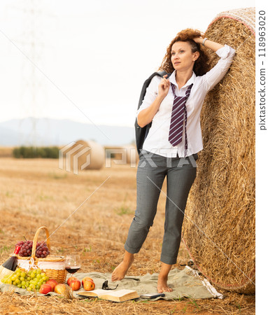 Young woman in white blouse and gray business suit standing on soft plaid mat near stack of straw 118963020