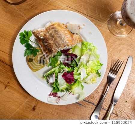 There is large piece of baked fish sea bass and salad of fresh vegetables on plate. There is large piece of baked fish sea bass and salad of fresh vegetables on plate. 118963034