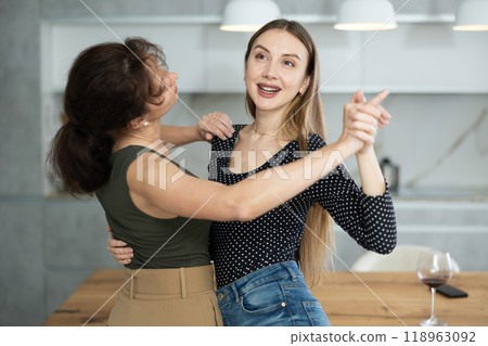 Two joyful middle-aged women dancing together at the kitchen-table with wineglasses Two joyful middle-aged women dancing together at the kitchen-table with wineglasses 118963092
