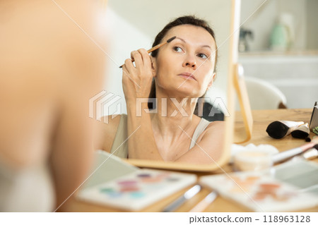 Woman applying eyebrow makeup with brush in front of mirror 118963128