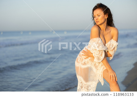 Woman in white negligee stands on coast 118963133