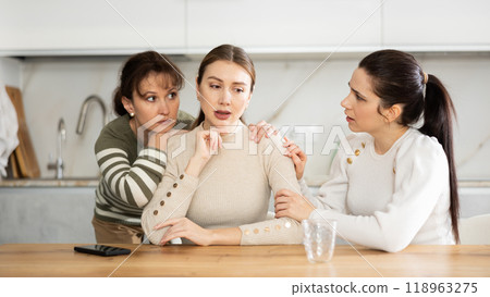 Sad middle-aged woman sitting at table while two others trying to calm her 118963275
