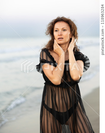 Woman in black negligee stands on coast 118963284