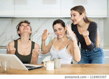 Three happy middle-aged woman expressing joy for winning in the kitchen 118963307