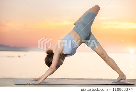 Near sea during sunset, girl performs Adho Mukha Svanasana Near sea during sunset, girl performs Adho Mukha Svanasana 118963374