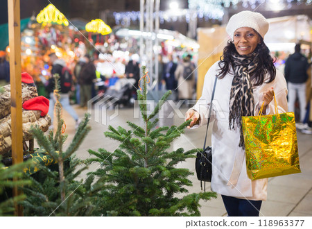 Positive woman choosing New Year's tree in christmas street fair 118963377