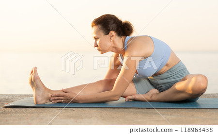 Near sea during sunset, girl performs variations of Janu Shirshasana Near sea during sunset, girl performs variations of Janu Shirshasana 118963438