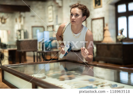 Woman observing artifacts inside glass display case at museum Woman observing artifacts inside glass display case at museum 118963518